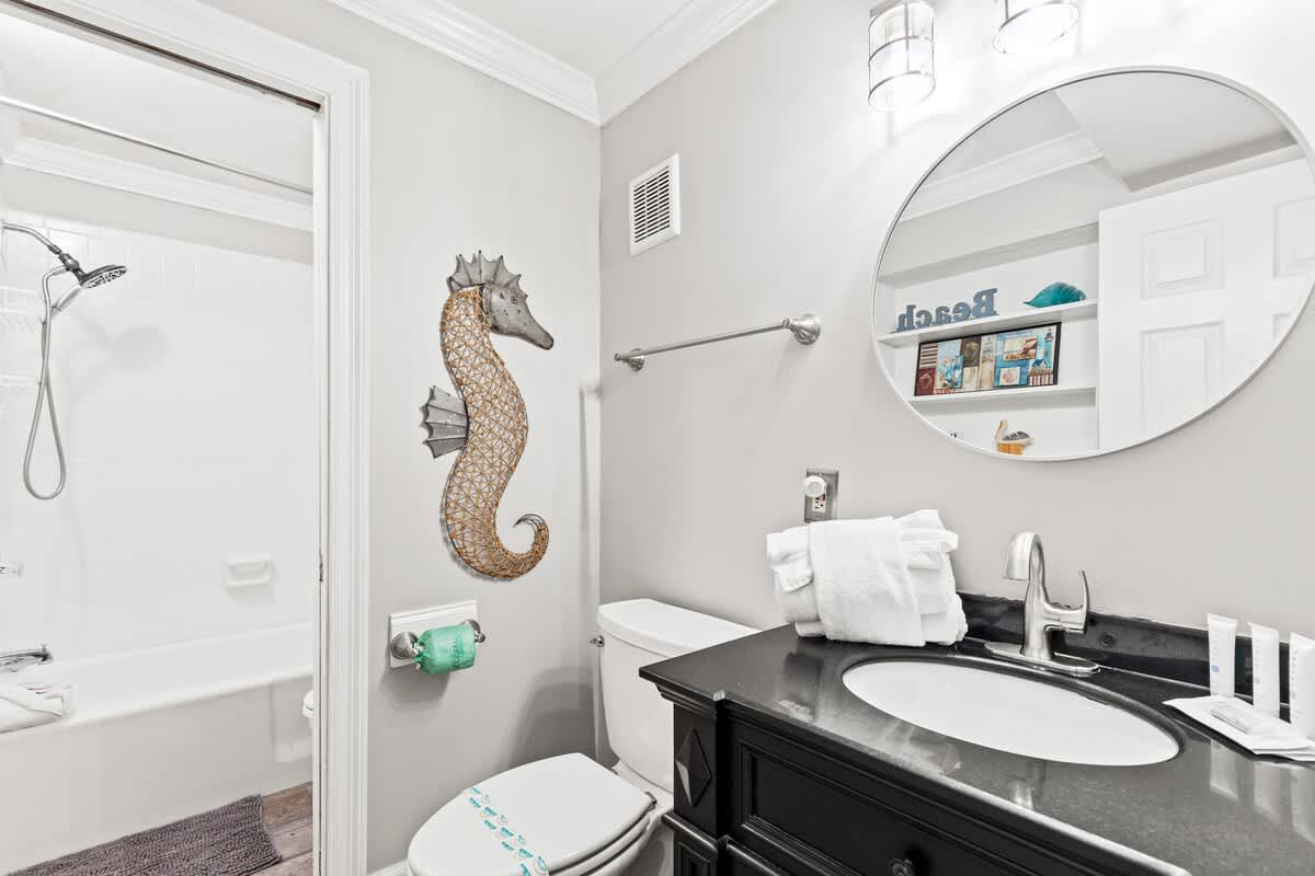 The Summit 1121 – Bathroom featuring a black vanity, circular mirror, seahorse wall decor, and a shower/tub combination.