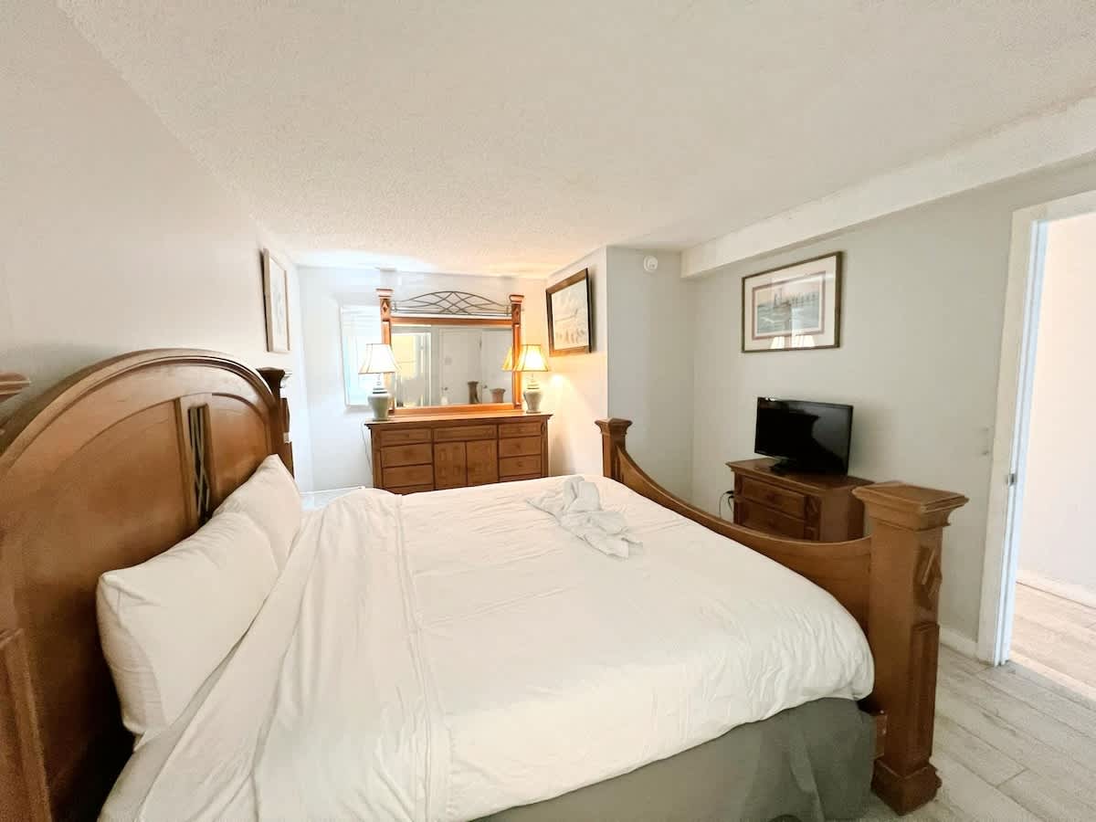 The Summit 618 – Bedroom with a wooden bed, dresser, mirror, TV, and two lamps.
