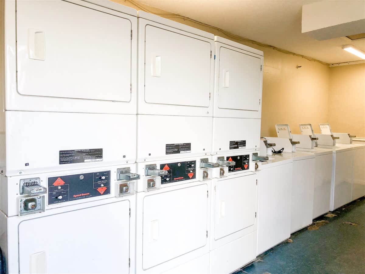 The Summit 618 – Laundry room with stacked dryers and washing machines against a beige wall.