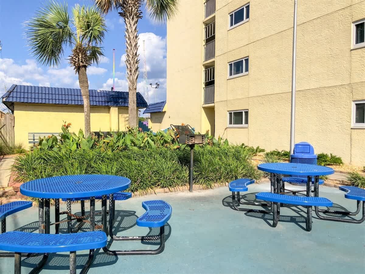 The Summit 618 – Outdoor seating area with blue picnic tables, palm trees, and nearby building walls.