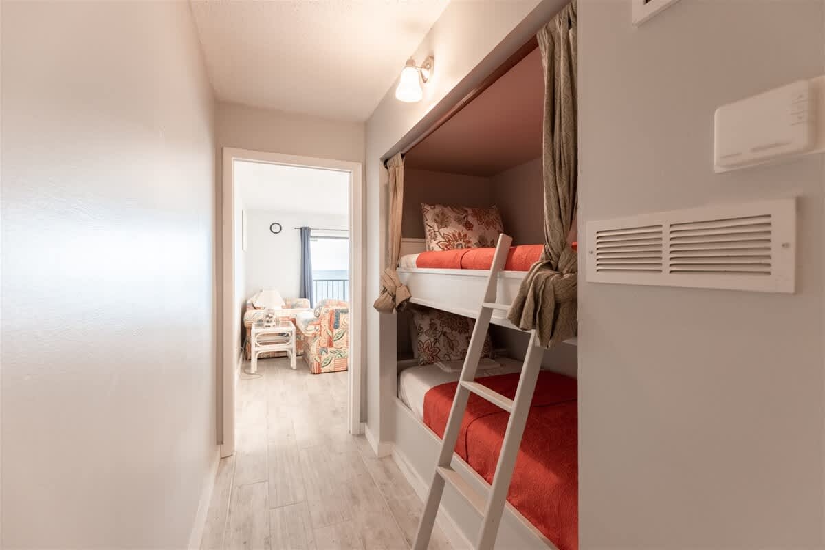The Summit 618 – Bunk bed area with red bedding and a view of a living space through an open doorway.