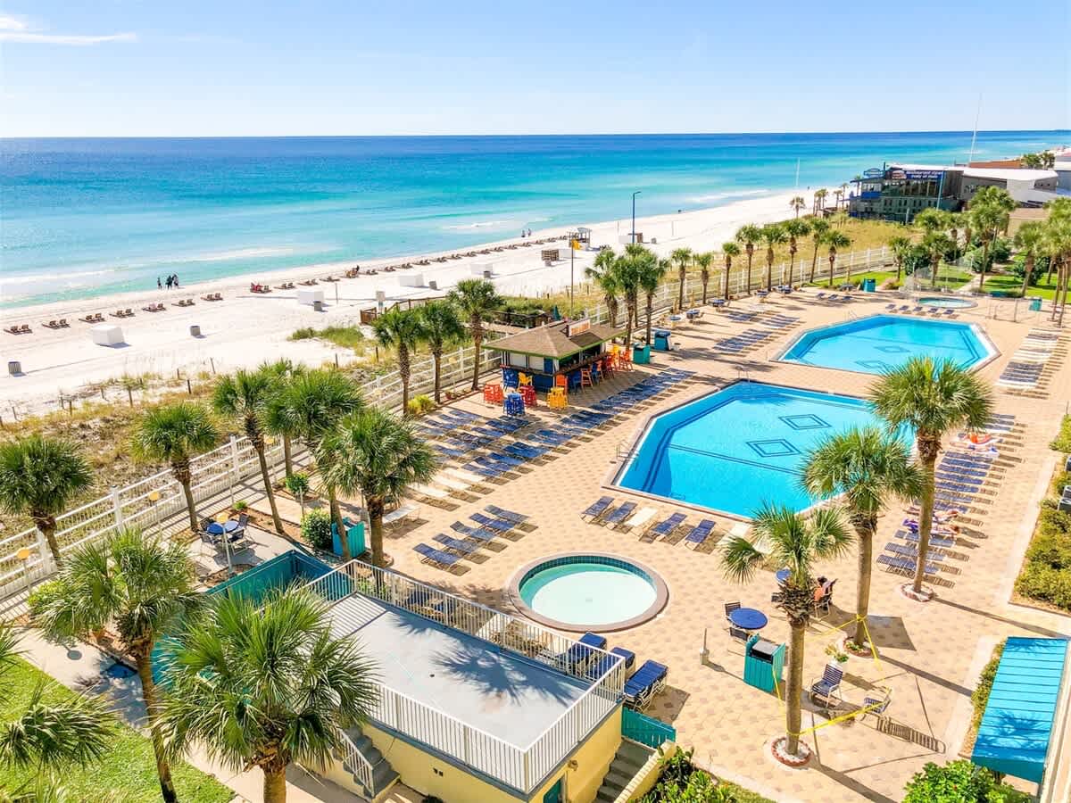 The Summit 618 – Aerial view of two pools, hot tub, palm trees, and beachfront.