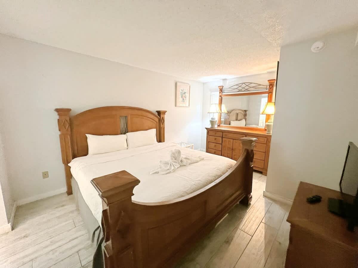 The Summit 618 – Bedroom with a wooden bed, dresser, lamps, and light-colored flooring.