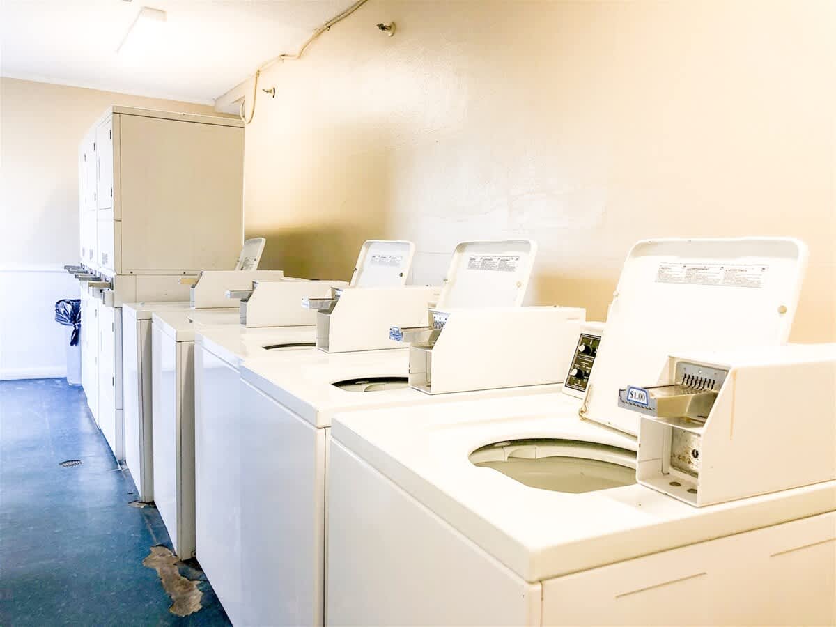 The Summit 618 – Laundry room with multiple white washing machines and drying machines against light-colored walls.