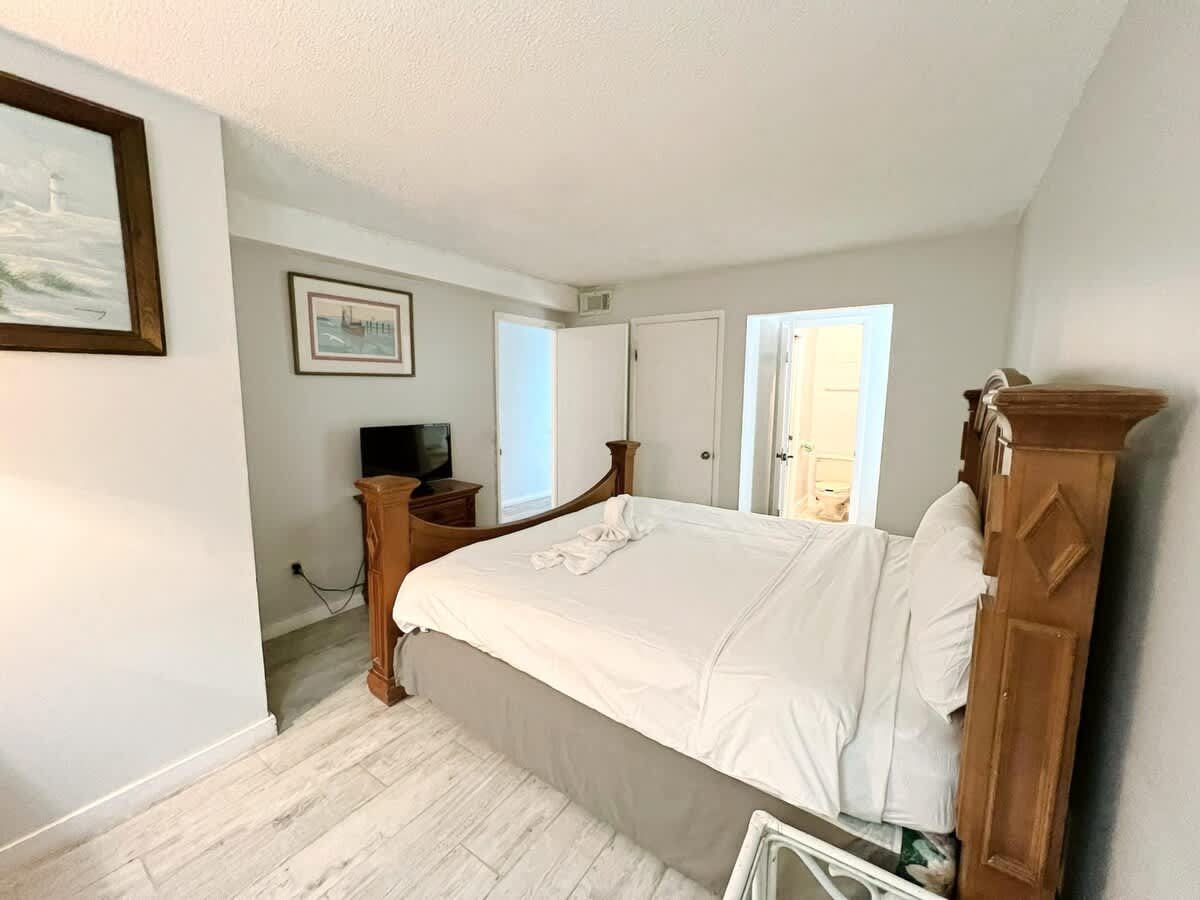 The Summit 618 – Bedroom with a wooden bed frame, TV, and a hallway leading to the bathroom.