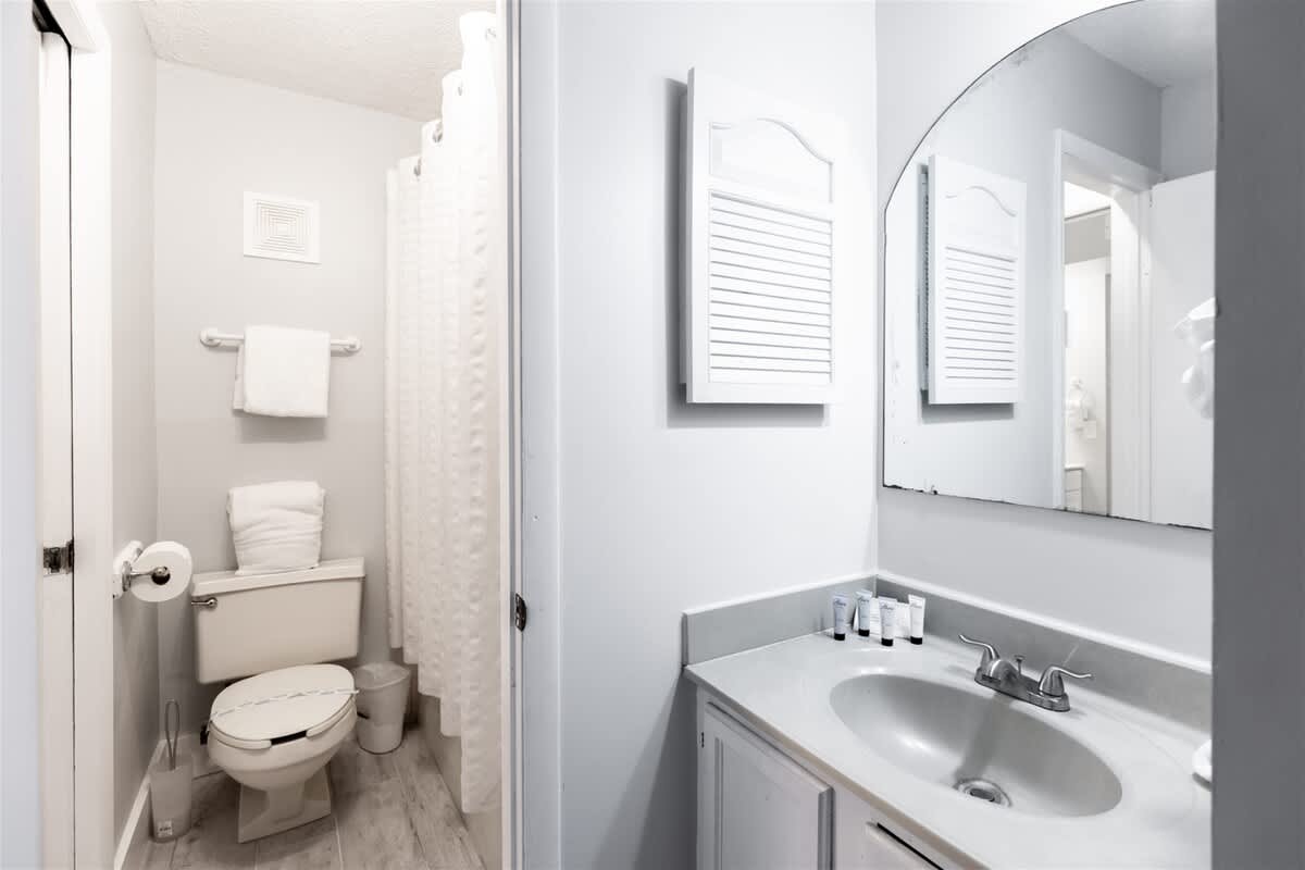 The Summit 618 – Bathroom with a sink, mirror, toilet, and shower curtain, featuring white towels and toiletries.