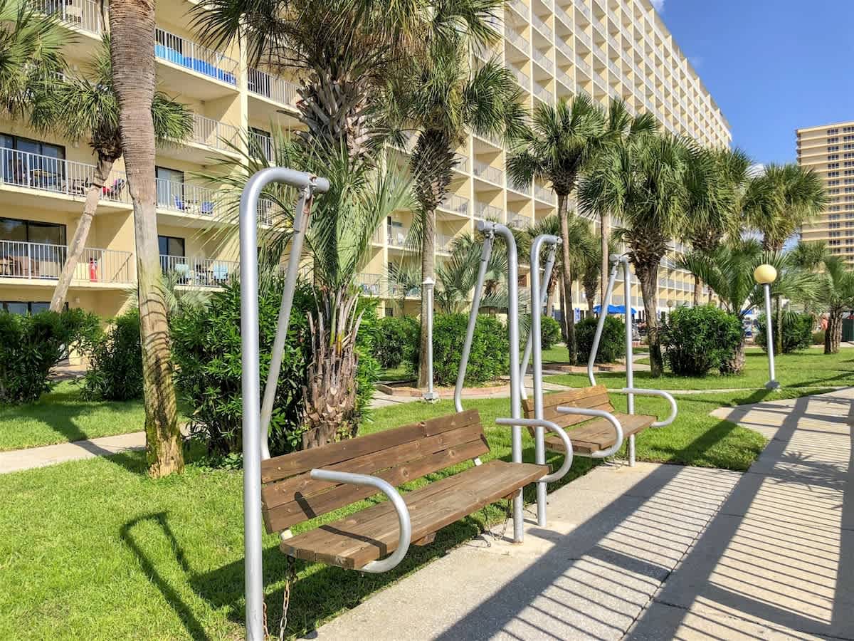 The Summit 618 – Exterior view of The Summit 618 with palm trees, benches, and balconies above greenery.