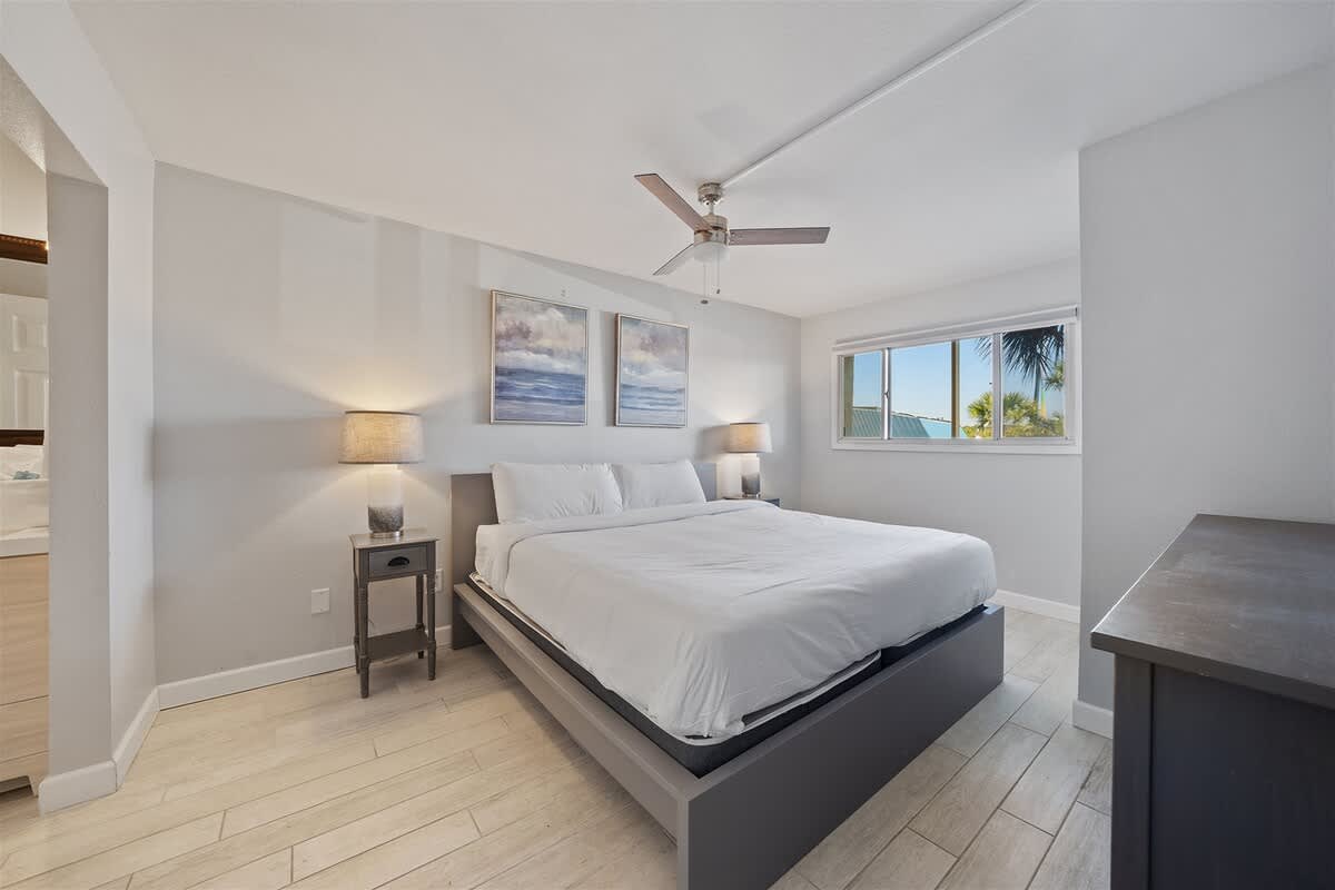 The Summit 220 – Bright bedroom with a king-sized bed, two lamps, and a window view of palm trees.
