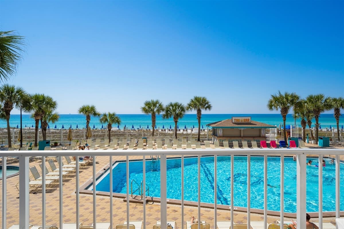 The Summit 220 – View from balcony showing pool, tiki bar, palm trees, and beach with turquoise water.