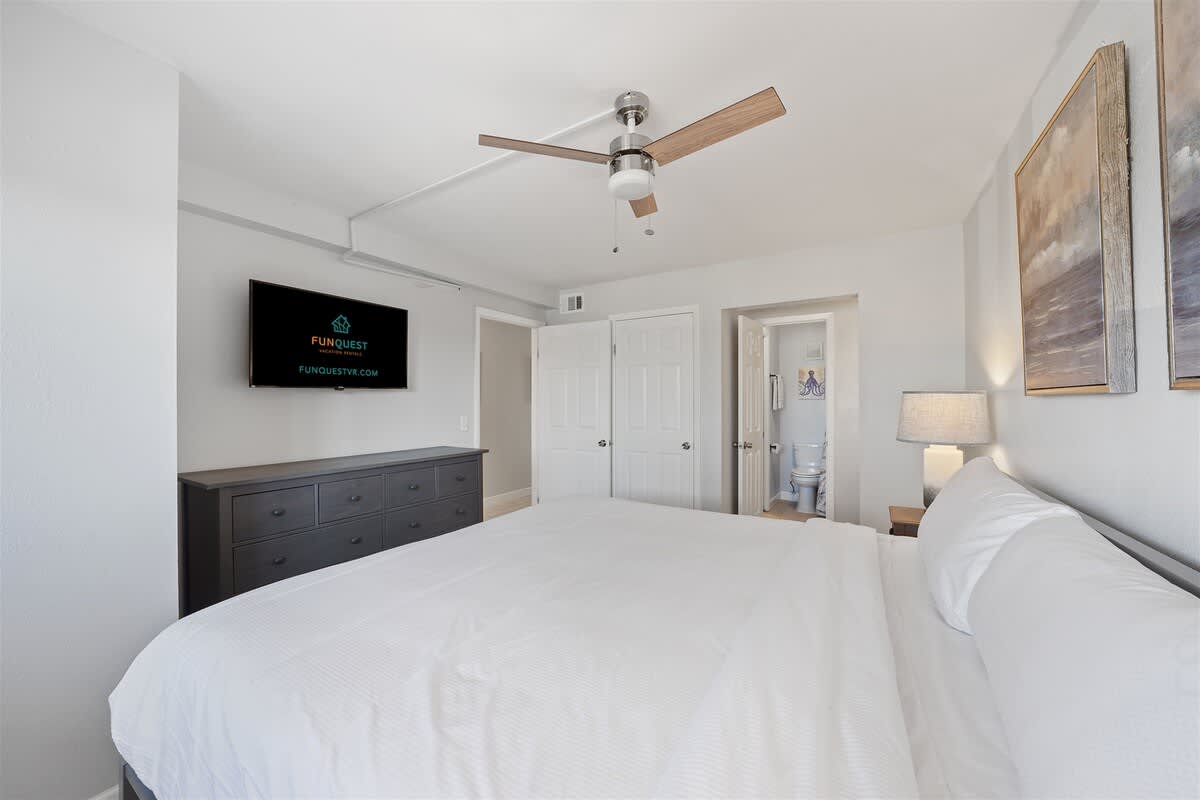 The Summit 220 – Bedroom with a king-size bed, dresser, TV, ceiling fan, and bathroom doorway visible.