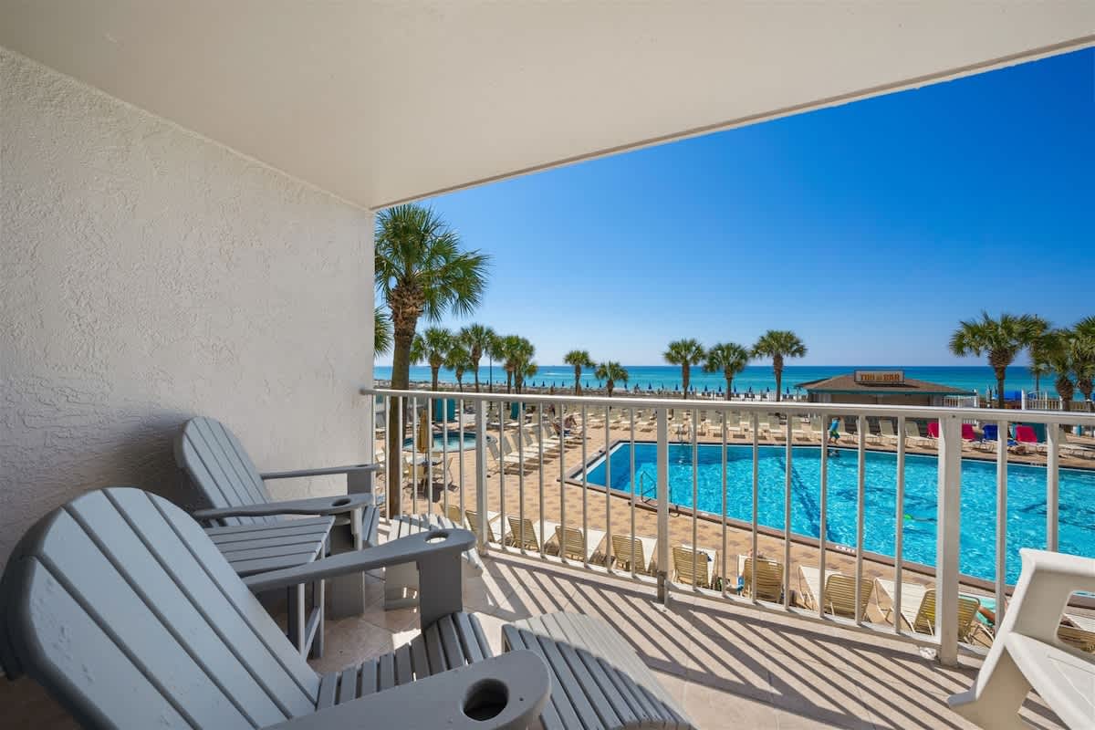 The Summit 220 – Balcony view of a pool area with palm trees and the ocean in the background.