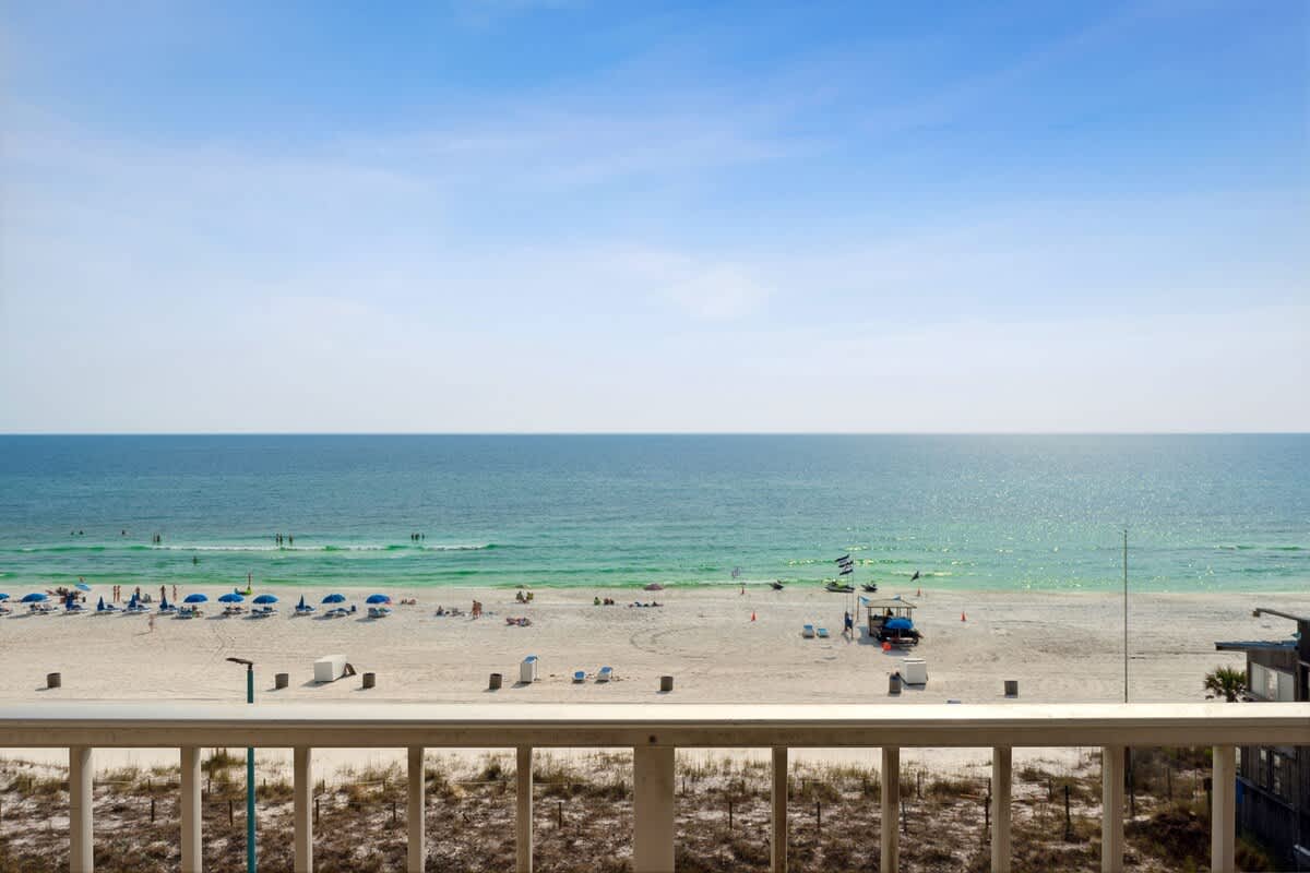 The Summit 602 – View from balcony overlooking sandy beach with umbrellas and people near the blue ocean.