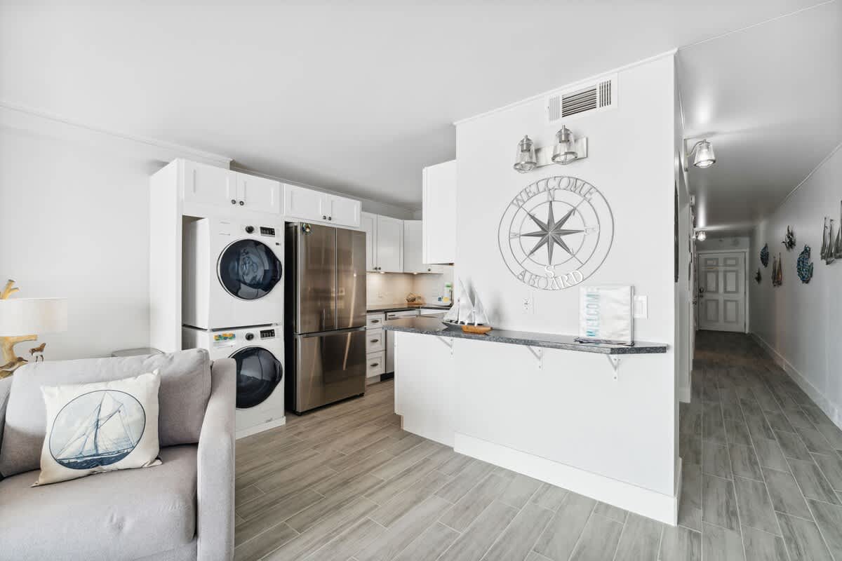The Summit 602 – Open kitchen area with washer-dryer, stainless steel appliances, and coastal decor accents.