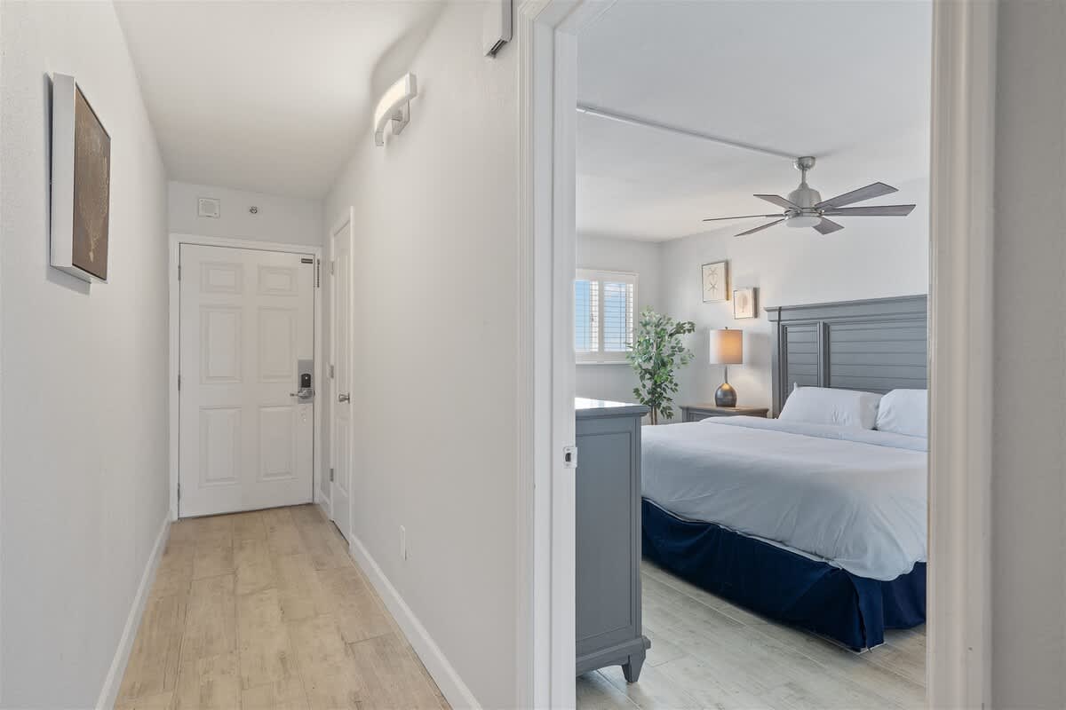 The Summit 621 – Hallway leading to a bedroom with a king-sized bed, ceiling fan, and window with blinds.