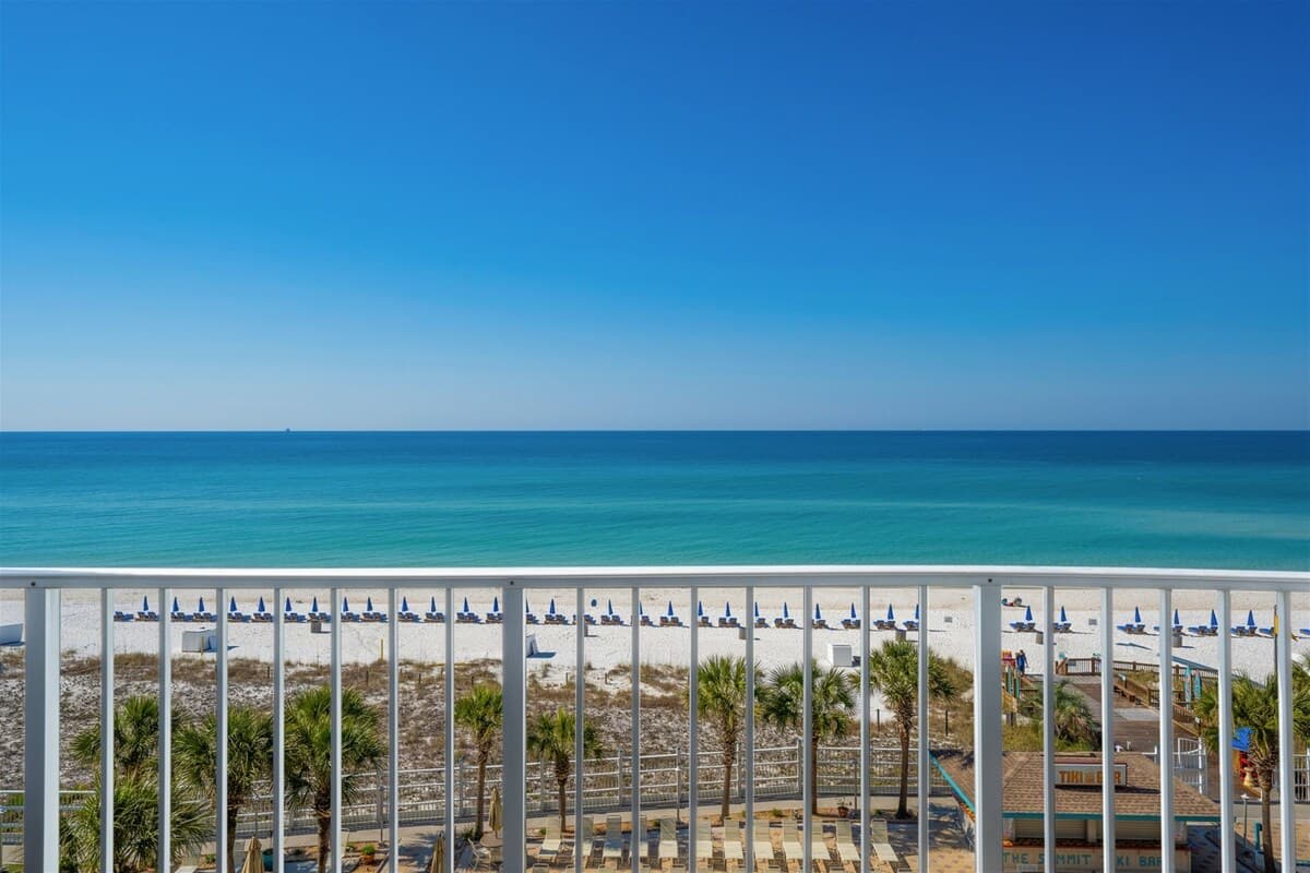 The Summit 621 – Balcony view of beach, umbrellas, clear blue ocean, and palm trees.