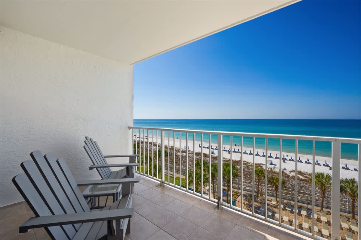 The Summit 621 – Balcony with two Adirondack chairs overlooking a sandy beach and clear blue water.
