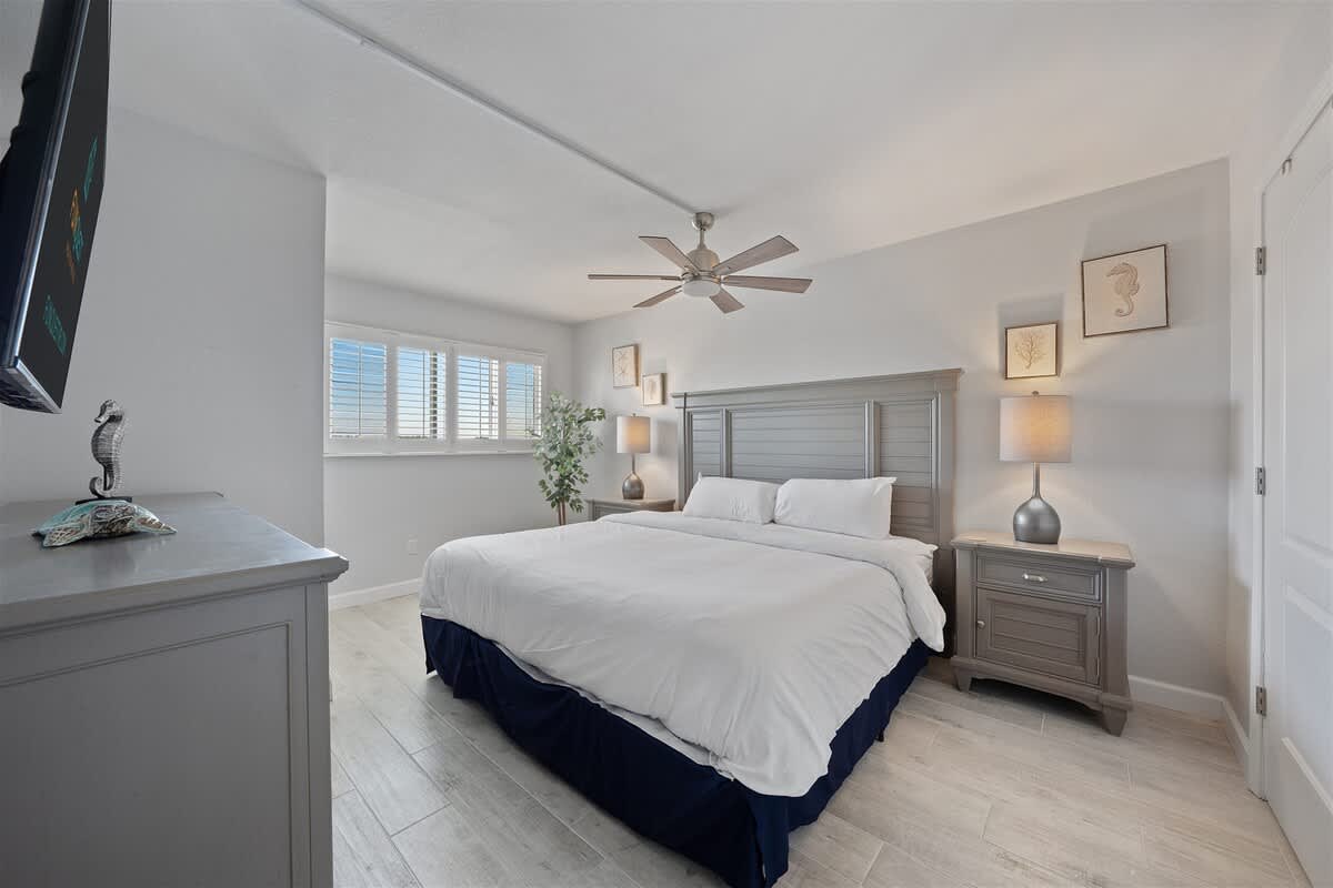 The Summit 621 – Bedroom with a king-size bed, ceiling fan, bedside table, and window with plantation shutters.