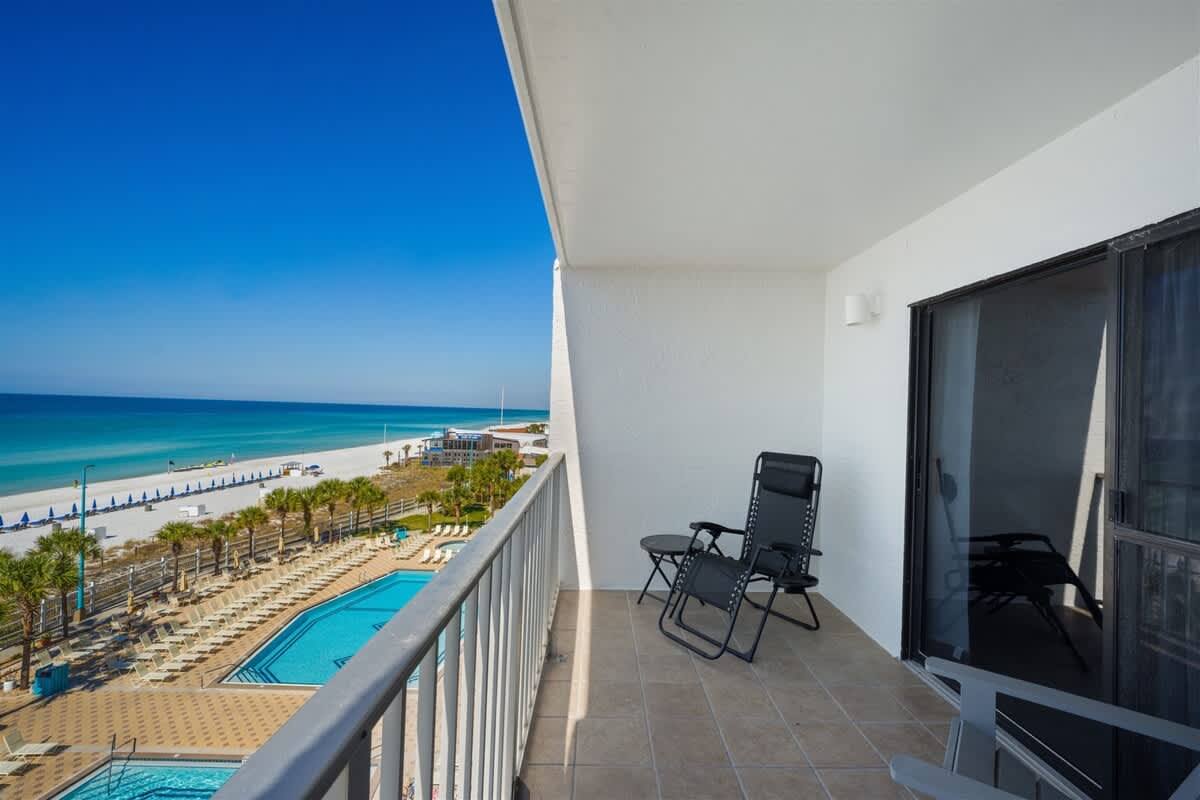 The Summit 621 – Balcony with two chairs overlooking a pool area and beachfront.