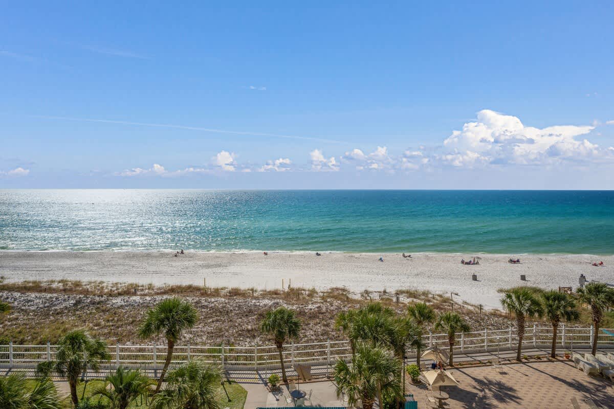 The Summit 624 – Ocean view from a balcony with palm trees, sandy beach, and distant beachgoers.