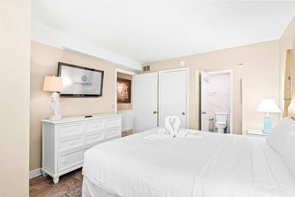 The Summit 820 – Bedroom with a queen bed, dresser, TV, lamp, and bathroom doorway.