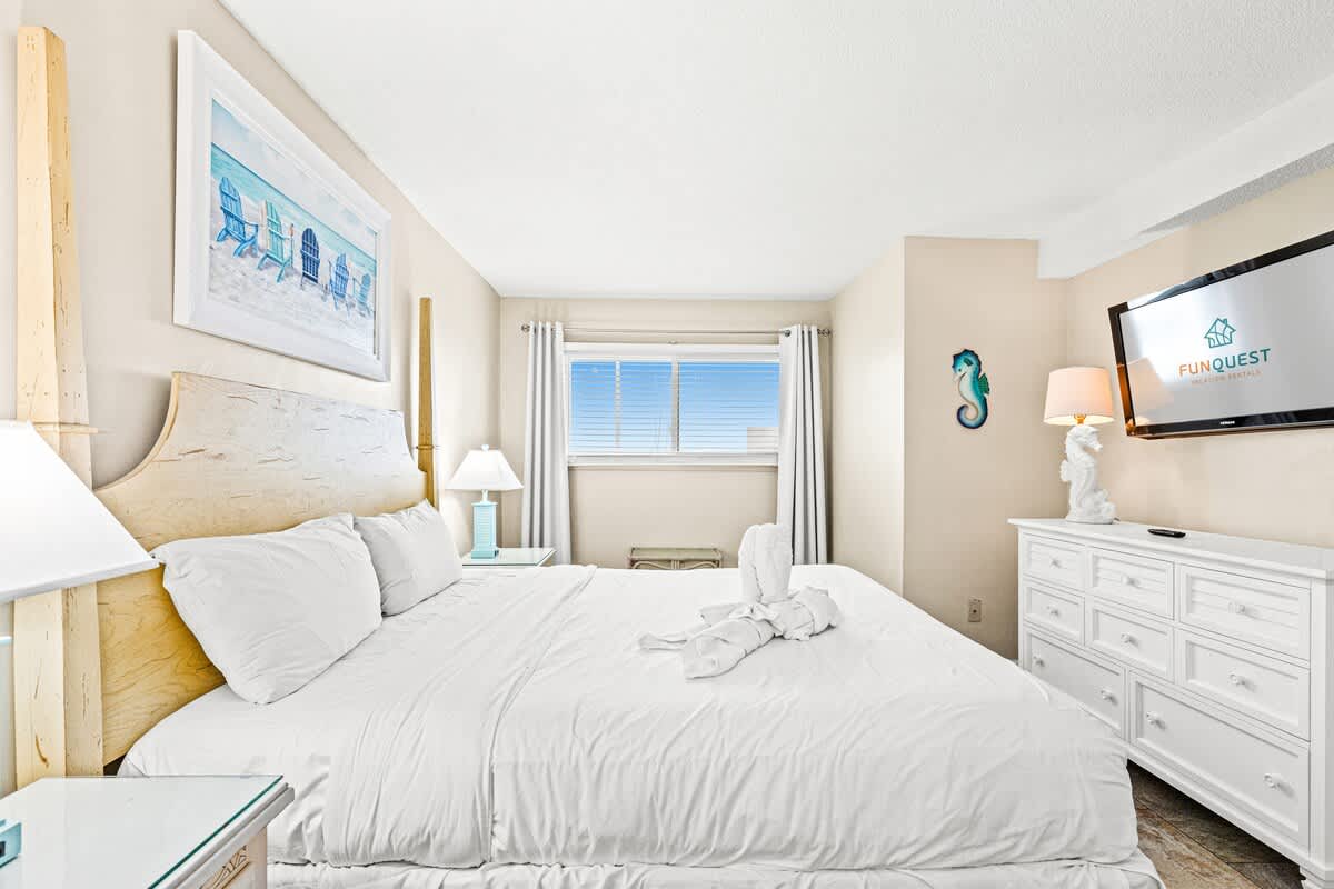 The Summit 820 – Bright bedroom with a king bed, dresser, TV, and window featuring a view of blue sky.