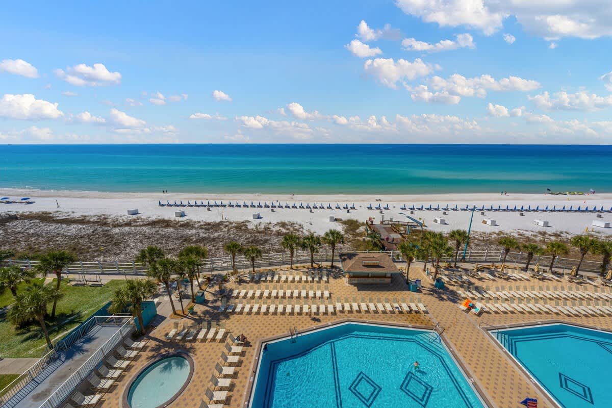 The Summit 820 – View of ocean, white sand beach, and swimming pools with lounge chairs in foreground.