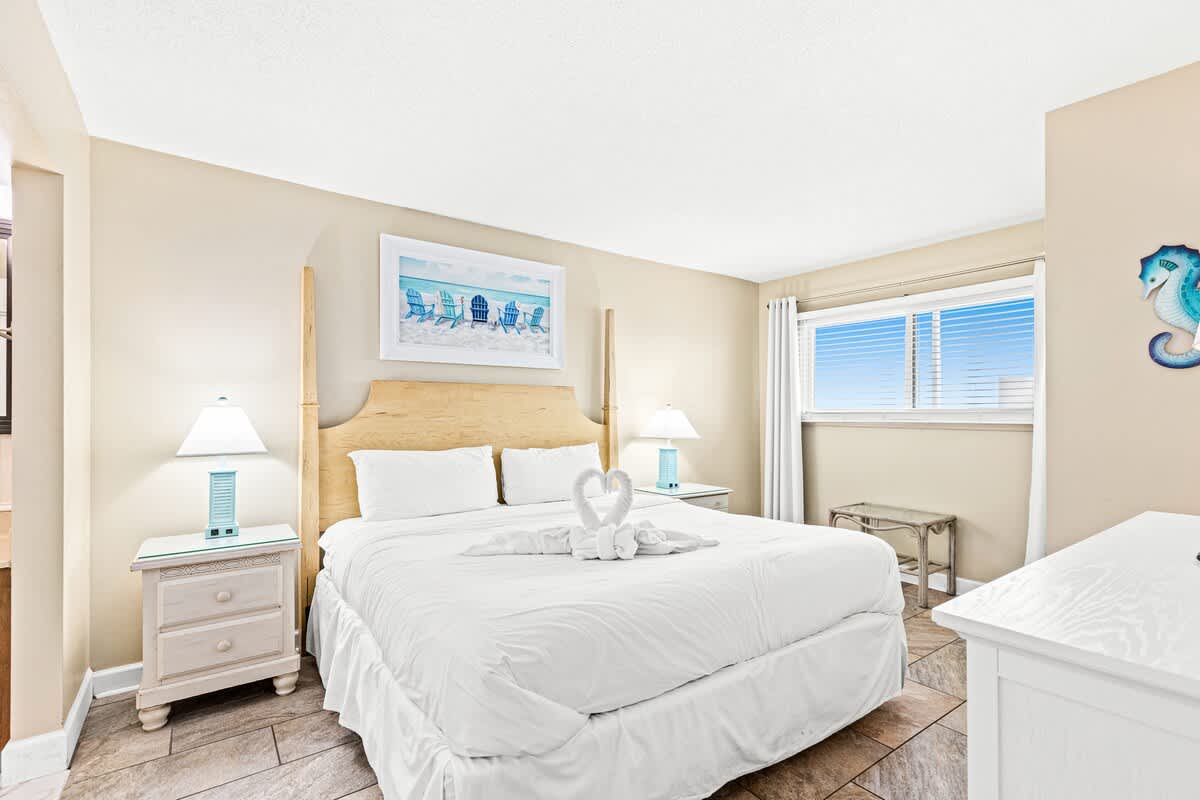 The Summit 820 – Cozy bedroom with a large bed, bedside tables, artwork, and a window with blinds.