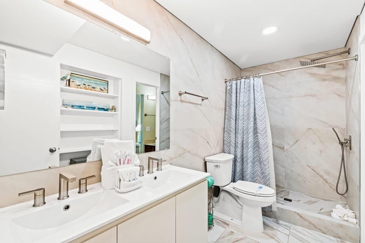 The Summit 820 – Modern bathroom with double sinks, shower, and decorative shelving. Light-colored tiles and a patterned shower curtain.