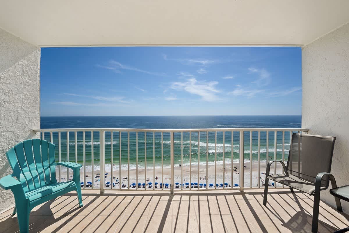The Summit 1408 – Balcony with turquoise chair overlooking the beach and ocean, bright blue sky.