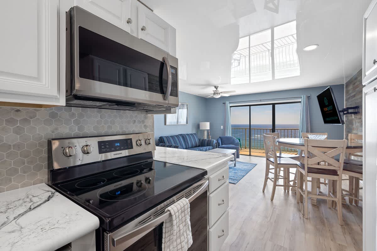 The Summit 1408 – Kitchen and living area with ocean view, featuring a dining table, couch, and TV.