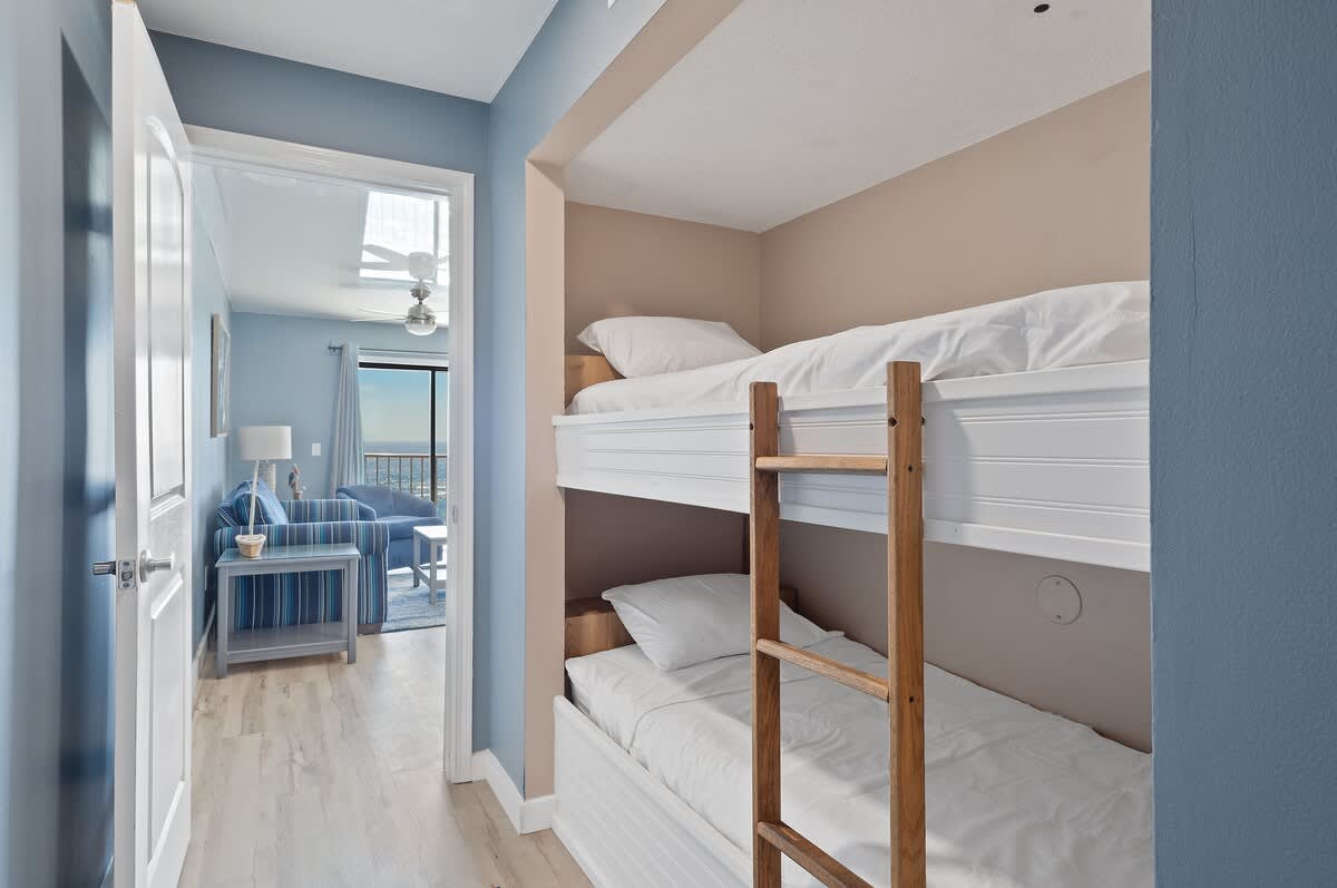 The Summit 1408 – Bunk bed nook with white bedding and a walkway leading to a living area with a view.