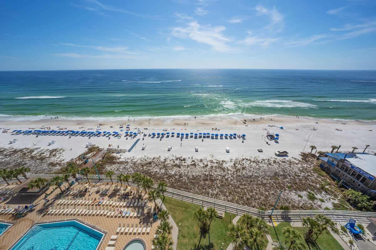 The Summit 1408 – Ocean view from balcony, featuring sandy beach, umbrellas, swimming pools, and palm trees.