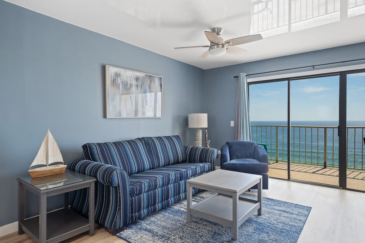 The Summit 1408 – Living area with blue walls, striped sofa, chair, and large windows showcasing an ocean view.