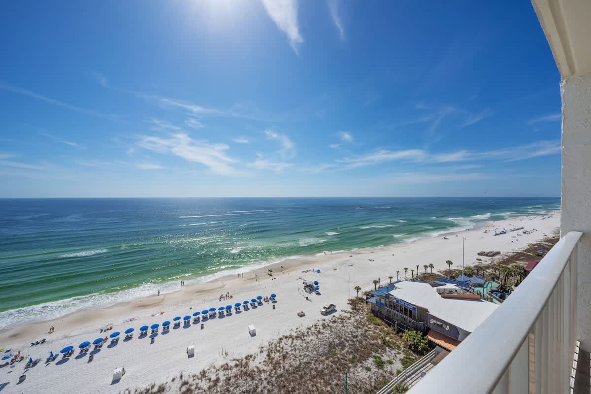 The Summit 1408 – Ocean view from balcony overlooking a sandy beach with umbrellas and waves. Bright sunny day.