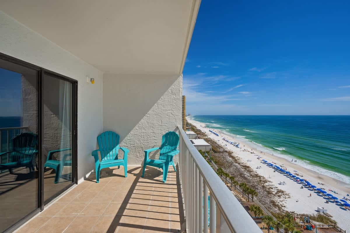 The Summit 1408 – Balcony with turquoise chairs overlooking a beach and ocean view.