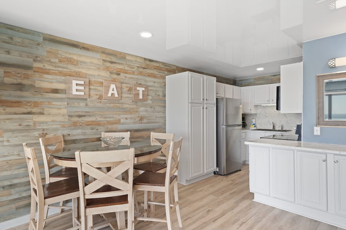 The Summit 1408 – Dining area with wooden table, white cabinetry, and stone accent wall in a modern kitchen setting.
