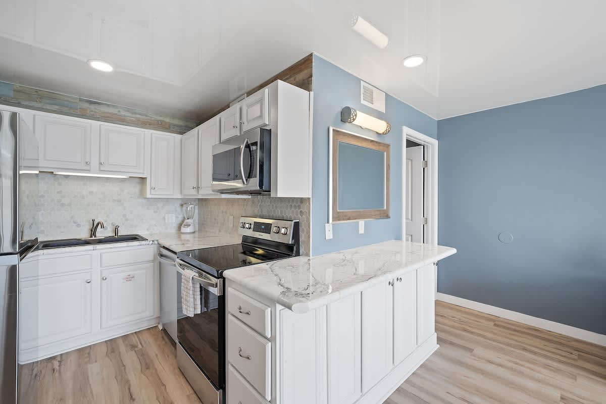 The Summit 1408 – Modern kitchen with white cabinets, stainless steel appliances, and a marble countertop. Blue accent wall visible.