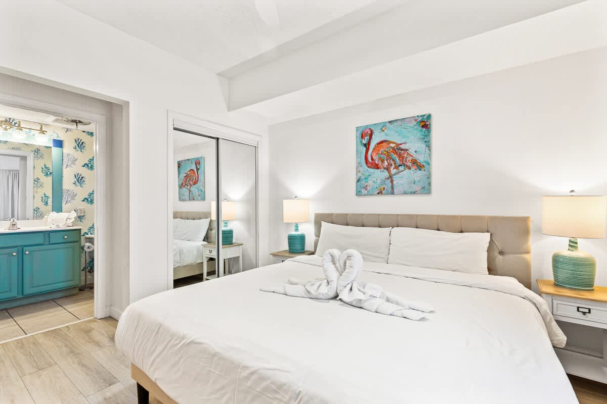 Seychelles 1006 – Cozy bedroom with a king-sized bed, colorful flamingo artwork, and an en-suite bathroom visible.