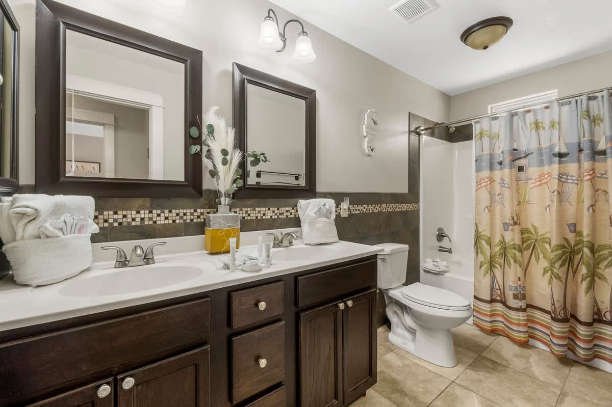 7405 Beach Dr A – Modern bathroom with double sinks, decorative mirrors, and a beach-themed shower curtain.