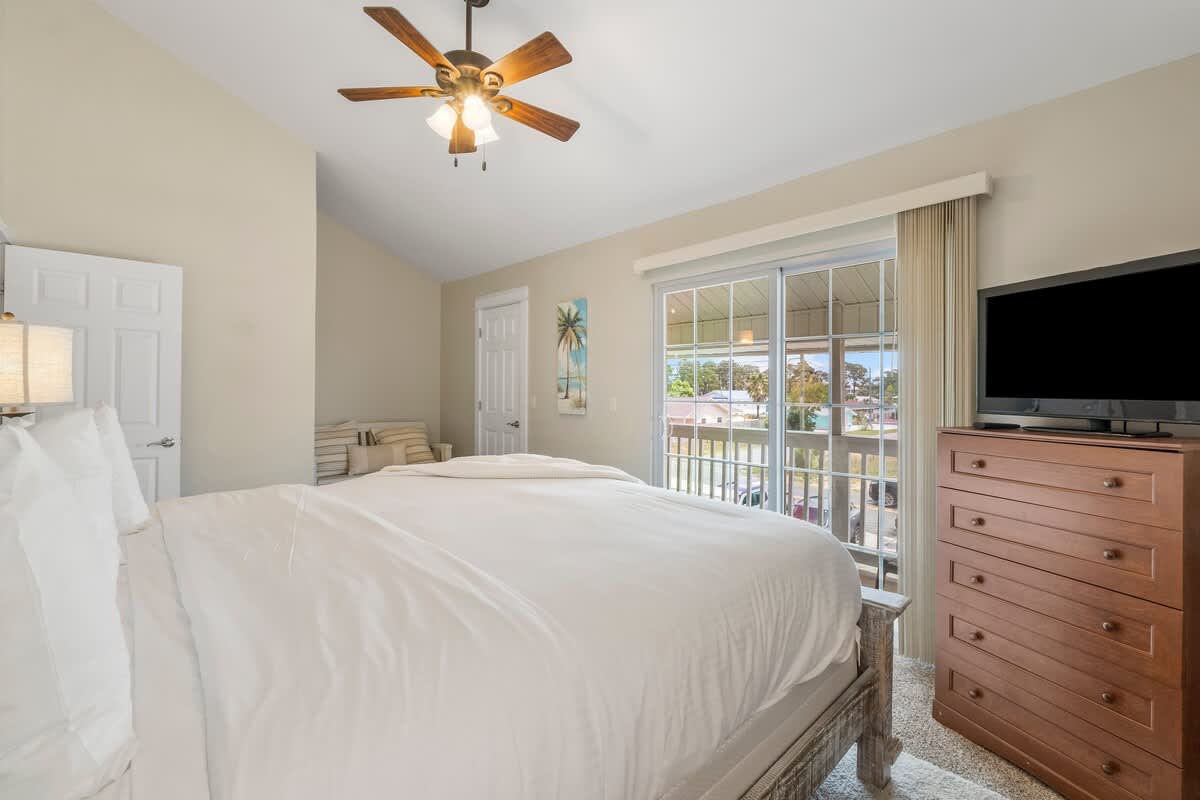 7405 Beach Dr A – Cozy bedroom with a king bed, dresser, ceiling fan, and balcony access.