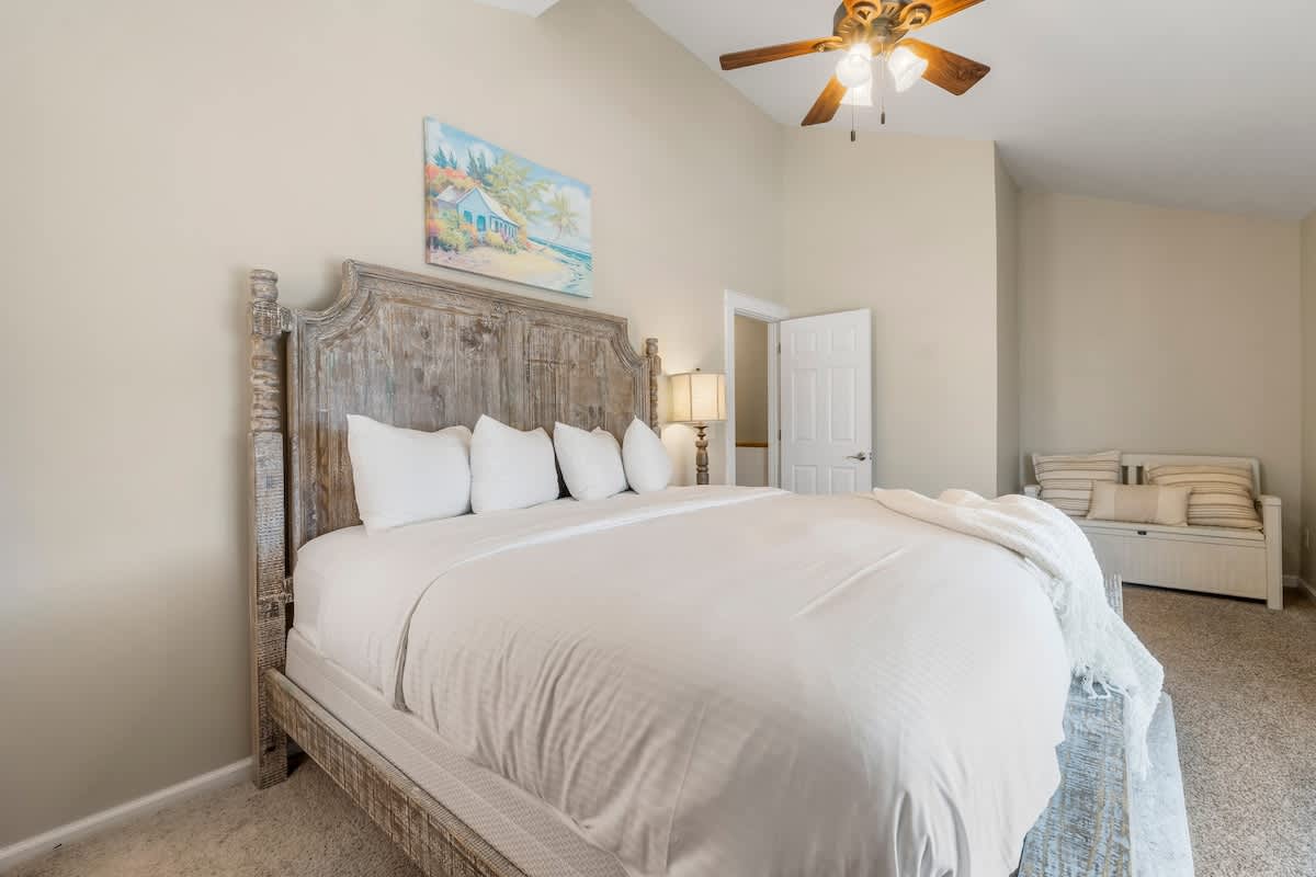 7405 Beach Dr A – Spacious bedroom with a large wooden bed, white linens, and a cozy seating area.