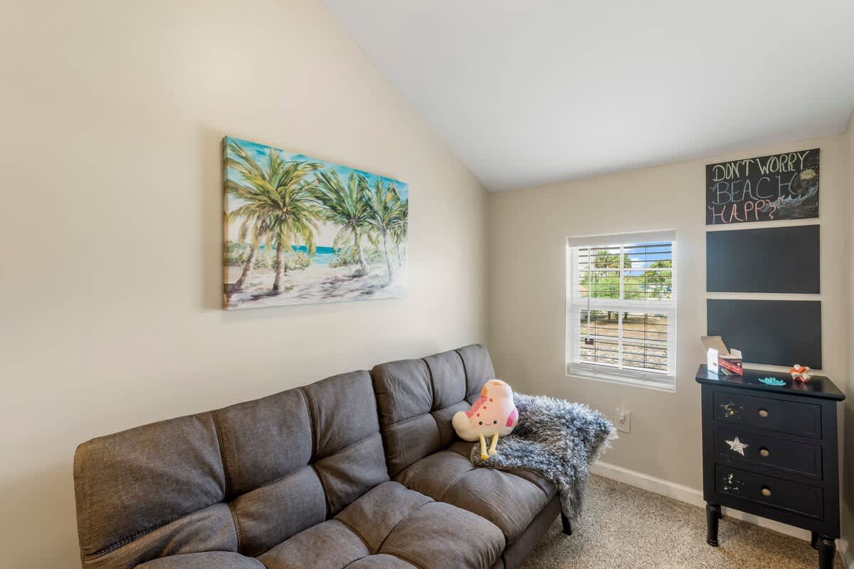 7405 Beach Dr A – Cozy living area with a gray couch, palm tree artwork, and a window with natural light.