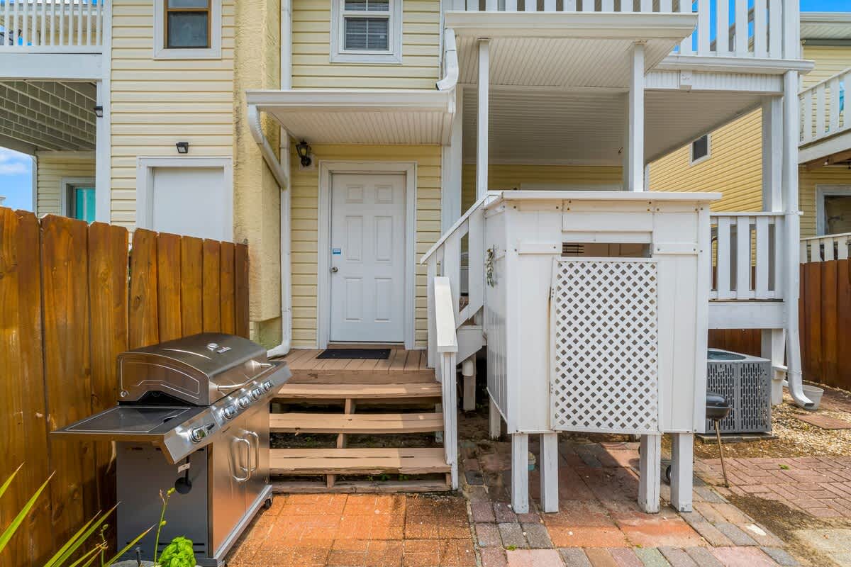 7405 Beach Dr A – Exterior view featuring a door, barbecue grill, wooden steps, and fenced yard area.