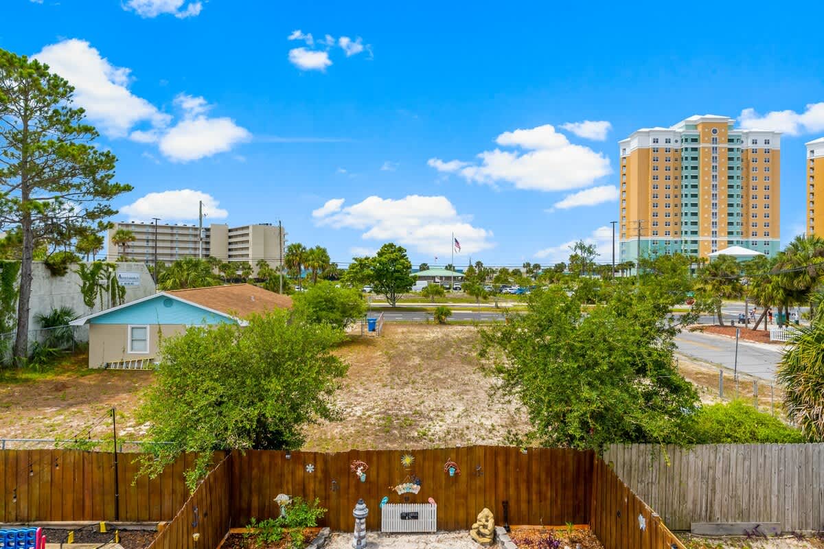 7405 Beach Dr A – View from a fenced backyard, featuring greenery and nearby buildings under a clear blue sky.