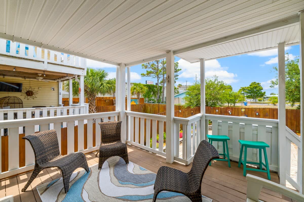 7405 Beach Dr A – Covered patio with woven chairs, a rug, and a view of greenery and distant buildings.
