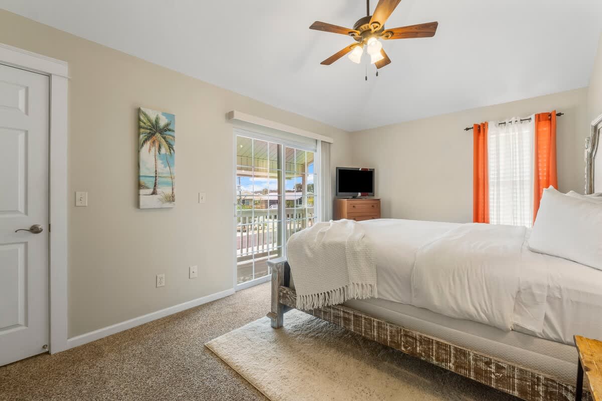7405 Beach Dr A – Cozy bedroom with a queen bed, television, and balcony access.