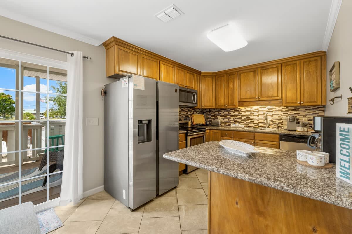 7405 Beach Dr A – Kitchen with stainless steel appliances, wooden cabinets, and a view of outdoor seating through a large window.