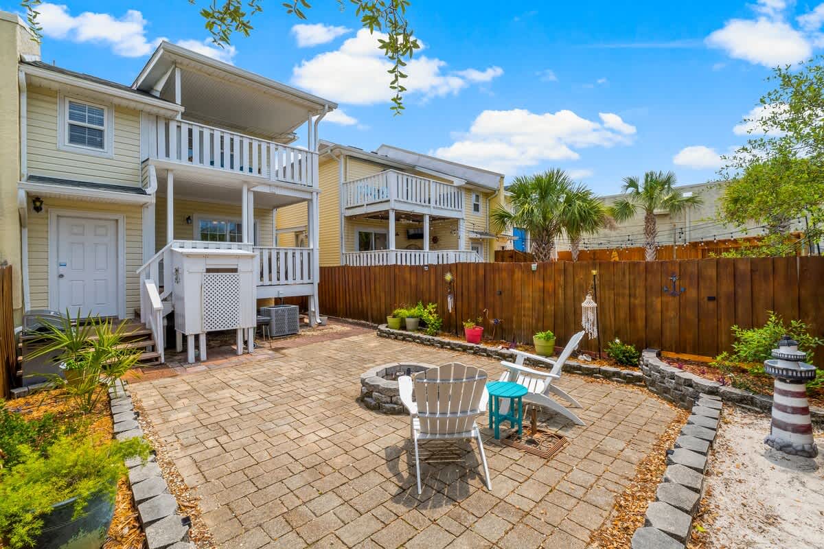 7405 Beach Dr A – Patio area with seating, fire pit, greenery, and neighboring houses under a blue sky.