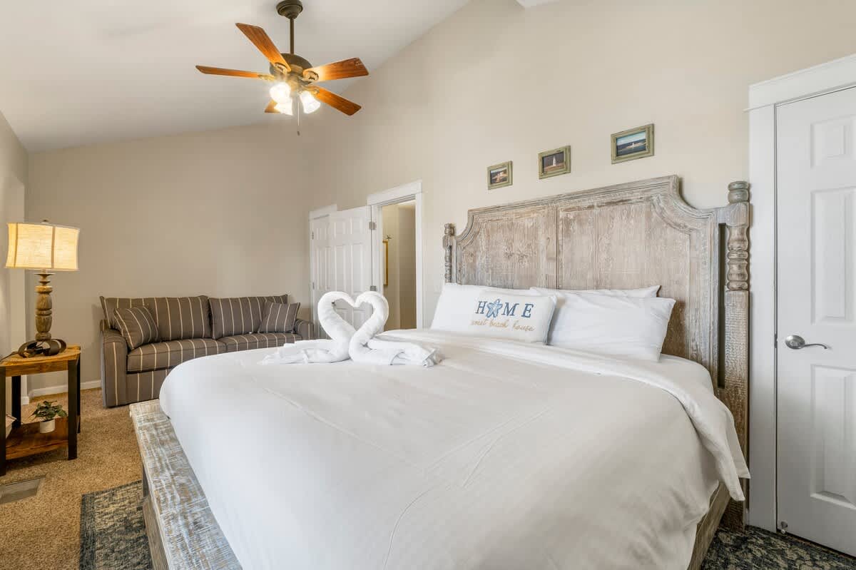 7405 Beach Dr A – Cozy bedroom with a large bed, couch, ceiling fan, and decorative artwork.