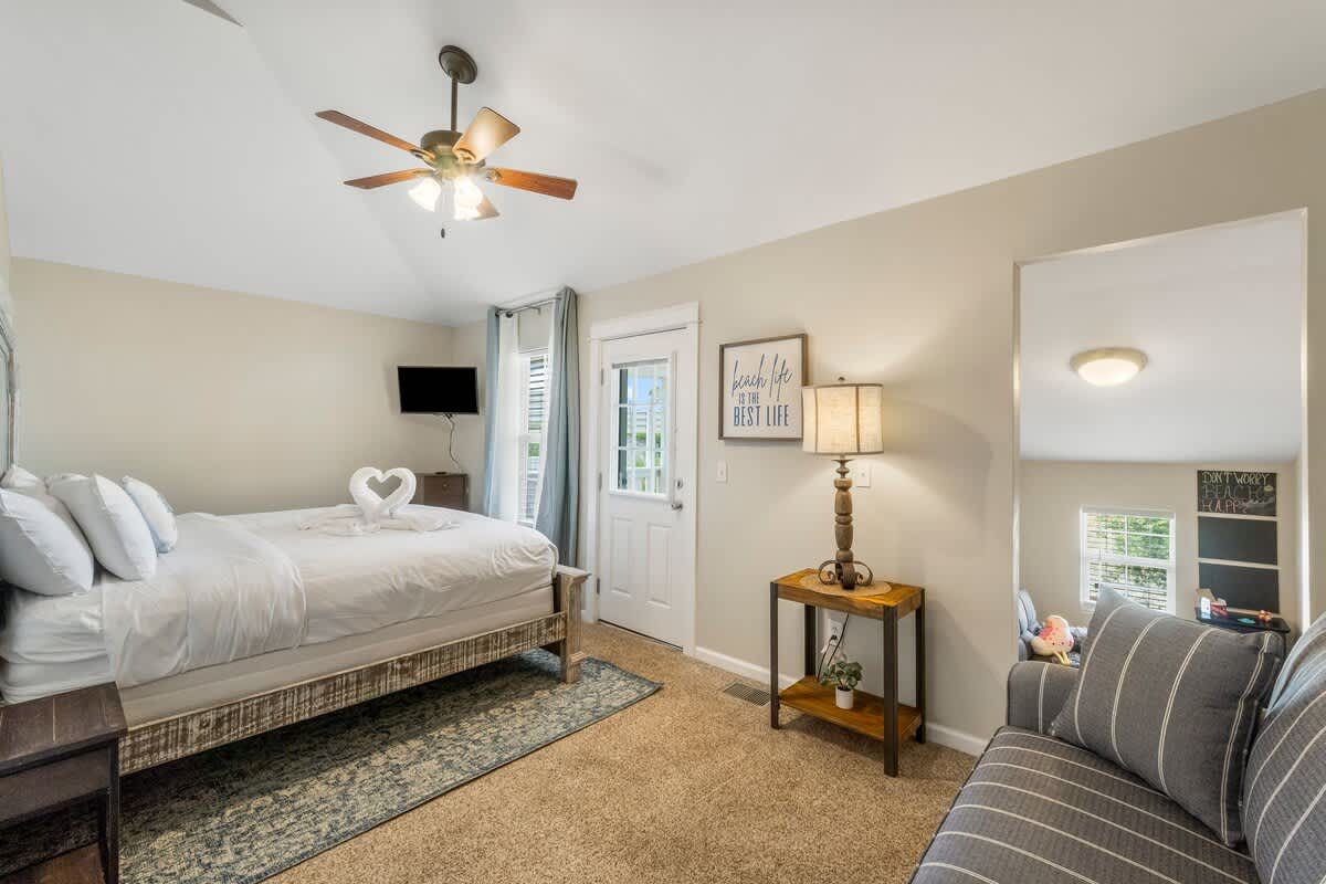 7405 Beach Dr A – Cozy bedroom with a queen bed, TV, seating area, and door leading outside.